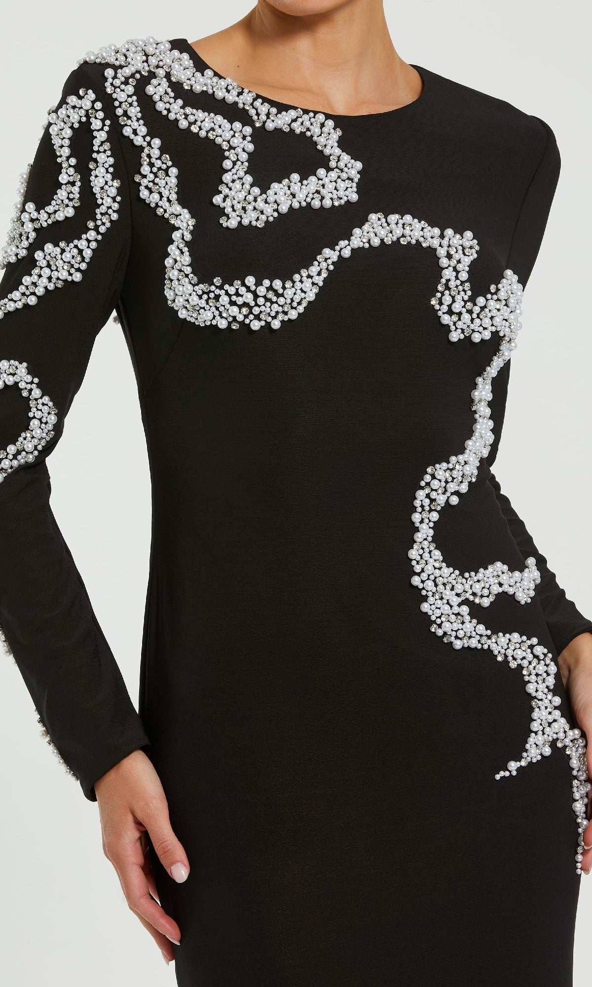 A person wearing the Mac Duggal 44086 Long Formal Dress, a black jersey evening gown featuring swirling white pearl patterns across the shoulder, chest, arm, and hip.